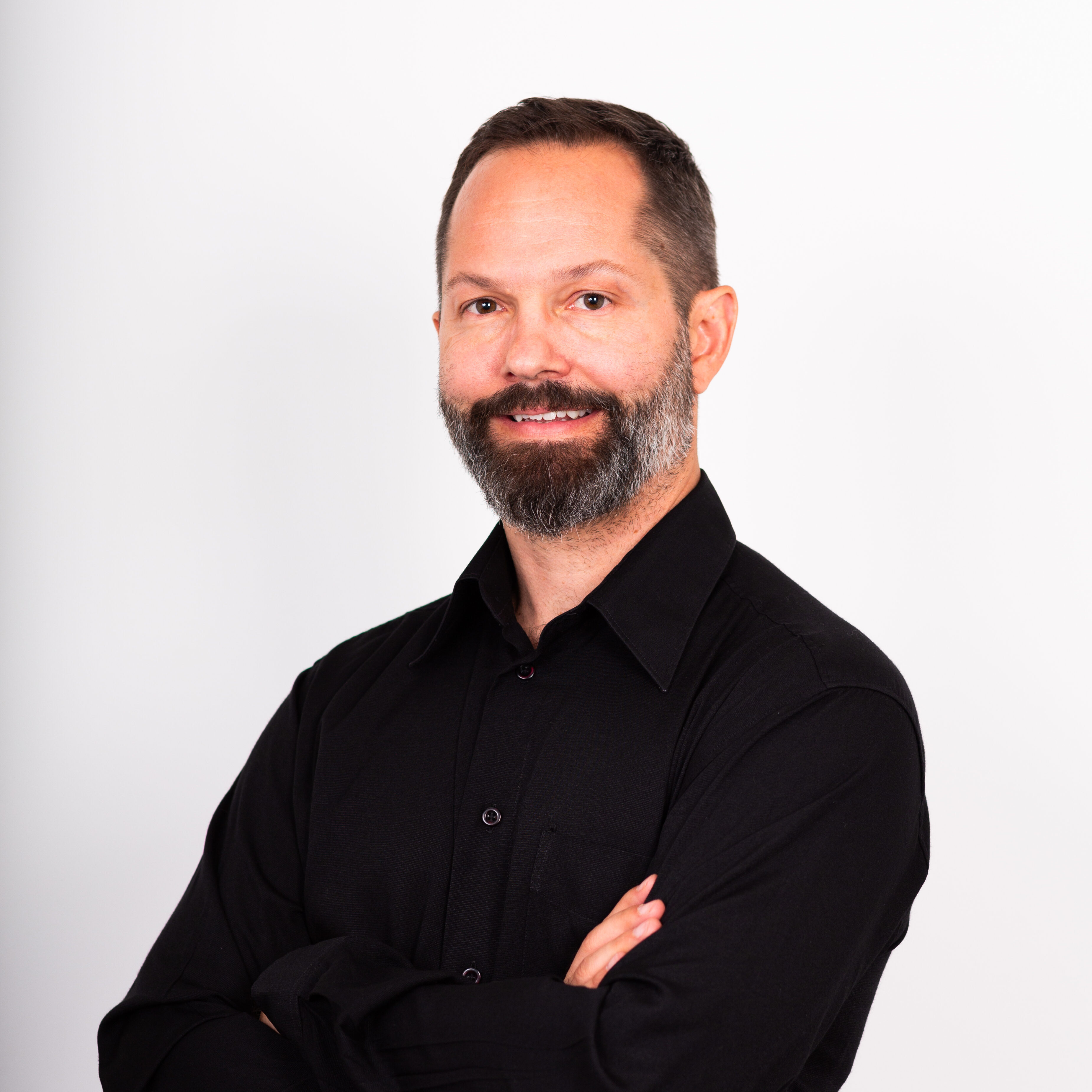 Person named Andreas in a black button-up shirt, arms crossed, smiling, against a white background.